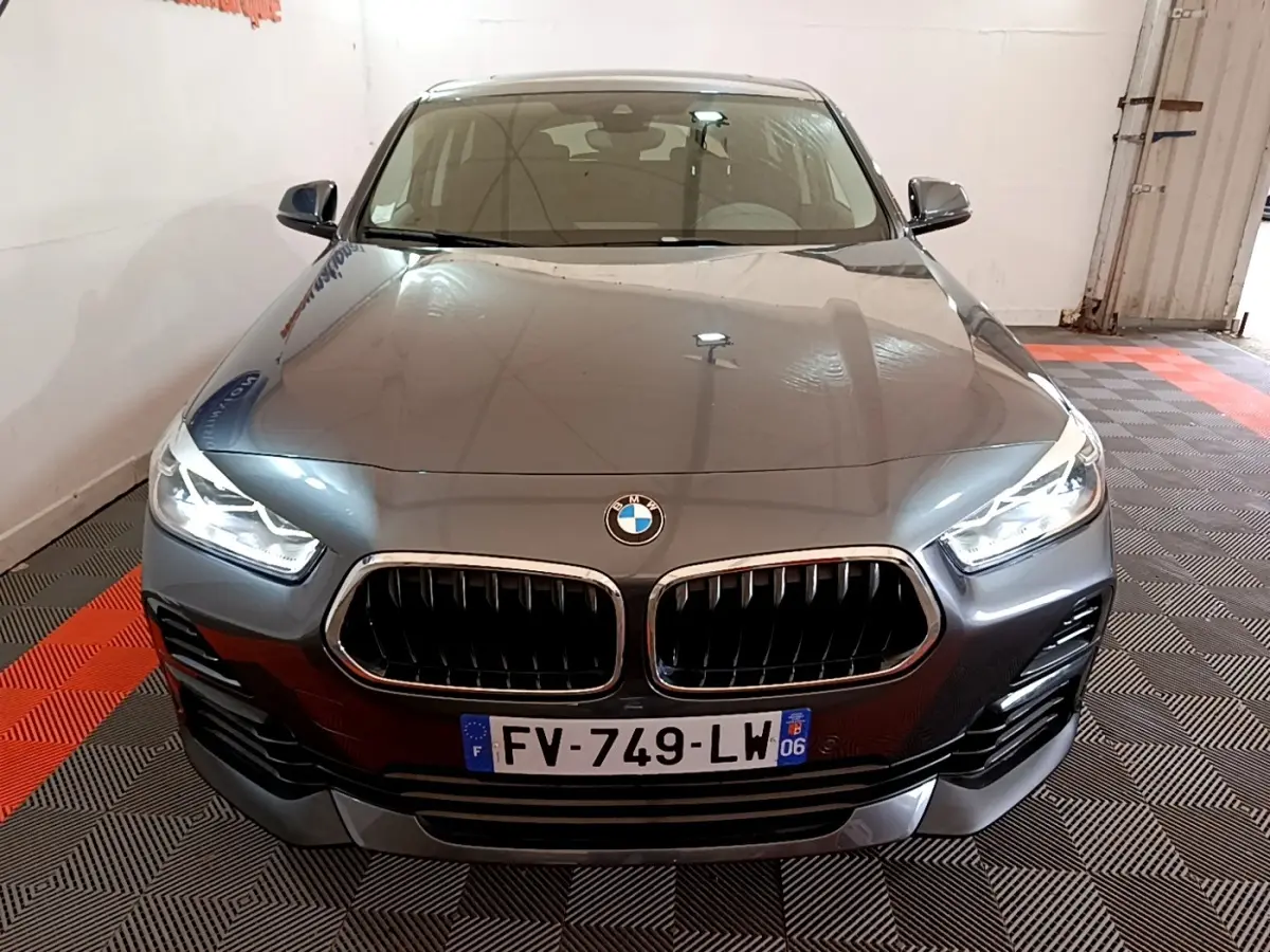 BMW X2 xDrive25e hybride rechargeable vue de face, couleur gris métallisé avec phares LED allumés dans un garage.
