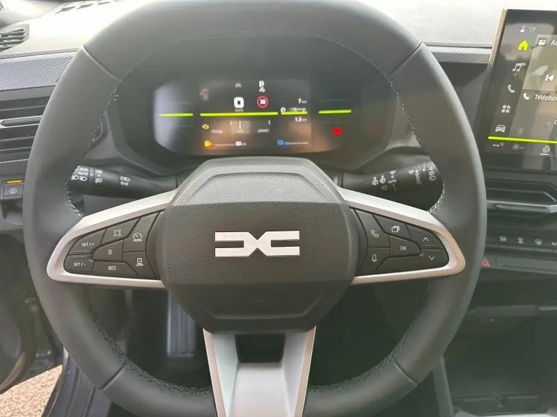 Vue rapprochée du volant multifonction du Dacia Duster 2025 hybride, avec tableau de bord numérique et écran tactile visible.