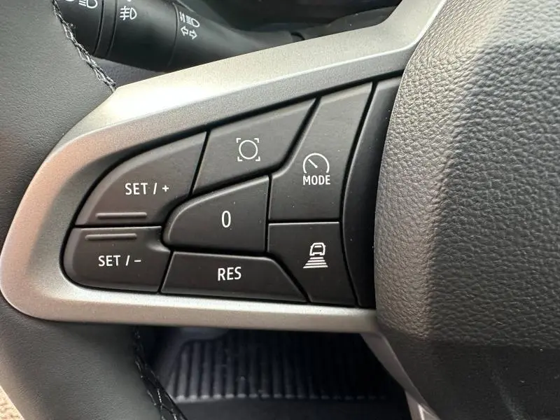 Gros plan sur les commandes au volant côté gauche du Dacia Duster 1.8 hybrid 155ch Journey, boutons noirs mat avec marquages blancs.