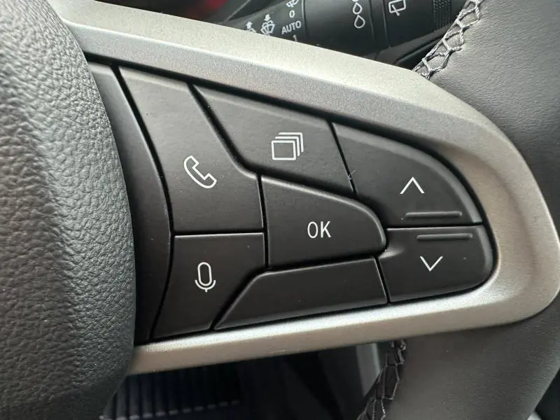Gros plan sur les commandes au volant côté gauche du Dacia Duster 1.8 hybrid 155ch Journey noir nacré, boutons multifonctions visibles.