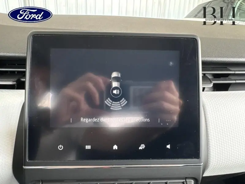 Écran tactile central affichant l'aide au stationnement d'une Renault Clio blanche, vue intérieure frontale.
