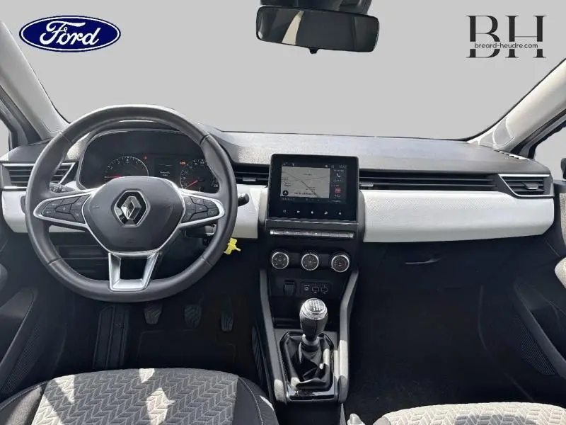 Vue intérieure avant du tableau de bord et volant noir d'une Renault Clio blanche, avec écran tactile et levier de vitesse manuel.
