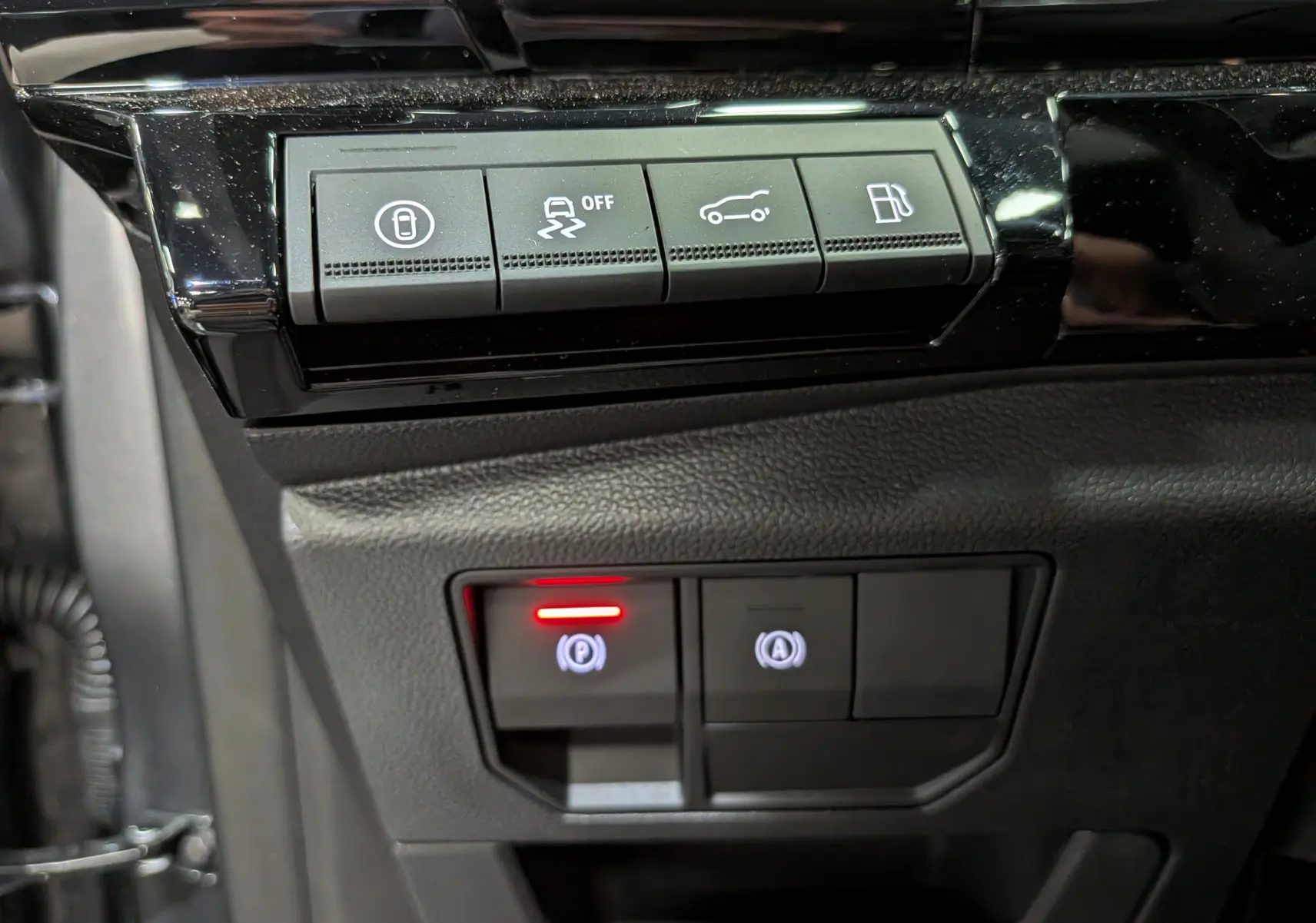 Gros plan sur les boutons de commande intérieurs noirs du Renault Rafale gris, avec témoin rouge d'activation du frein à main.