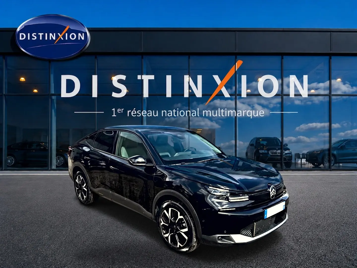 Vue 3/4 avant gauche d'une Citroën C4 X noire 2025 avec jantes alu et calandre distinctive devant un showroom Distinxion.