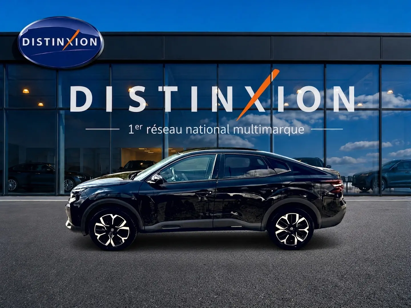 Vue de profil côté gauche d'une Citroën C4 X noire 2025 devant une vitrine avec logo Distinxion.