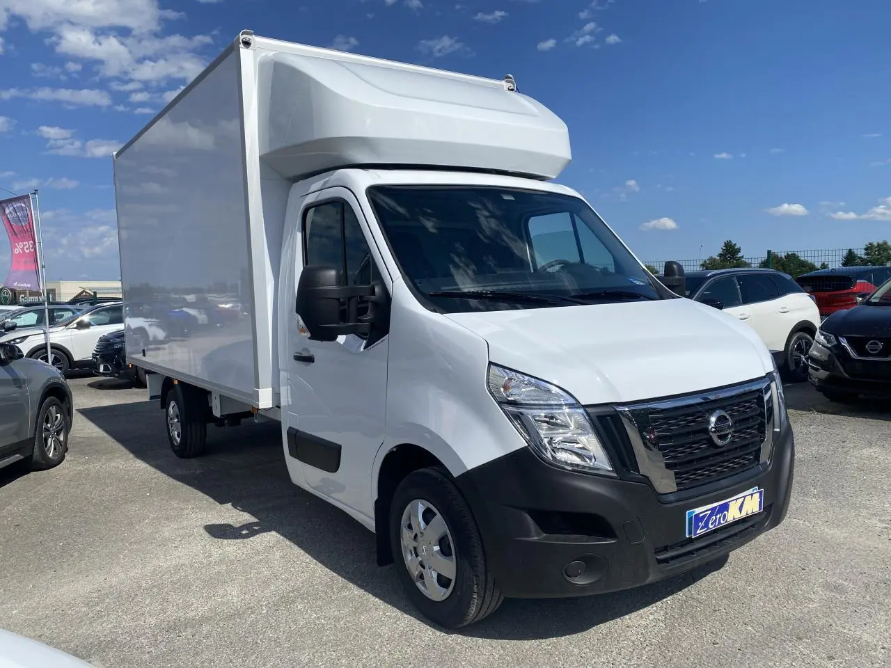 Vue 3/4 avant droite d’un utilitaire Nissan Interstar blanc avec capucine, stationné en extérieur sous ciel bleu.