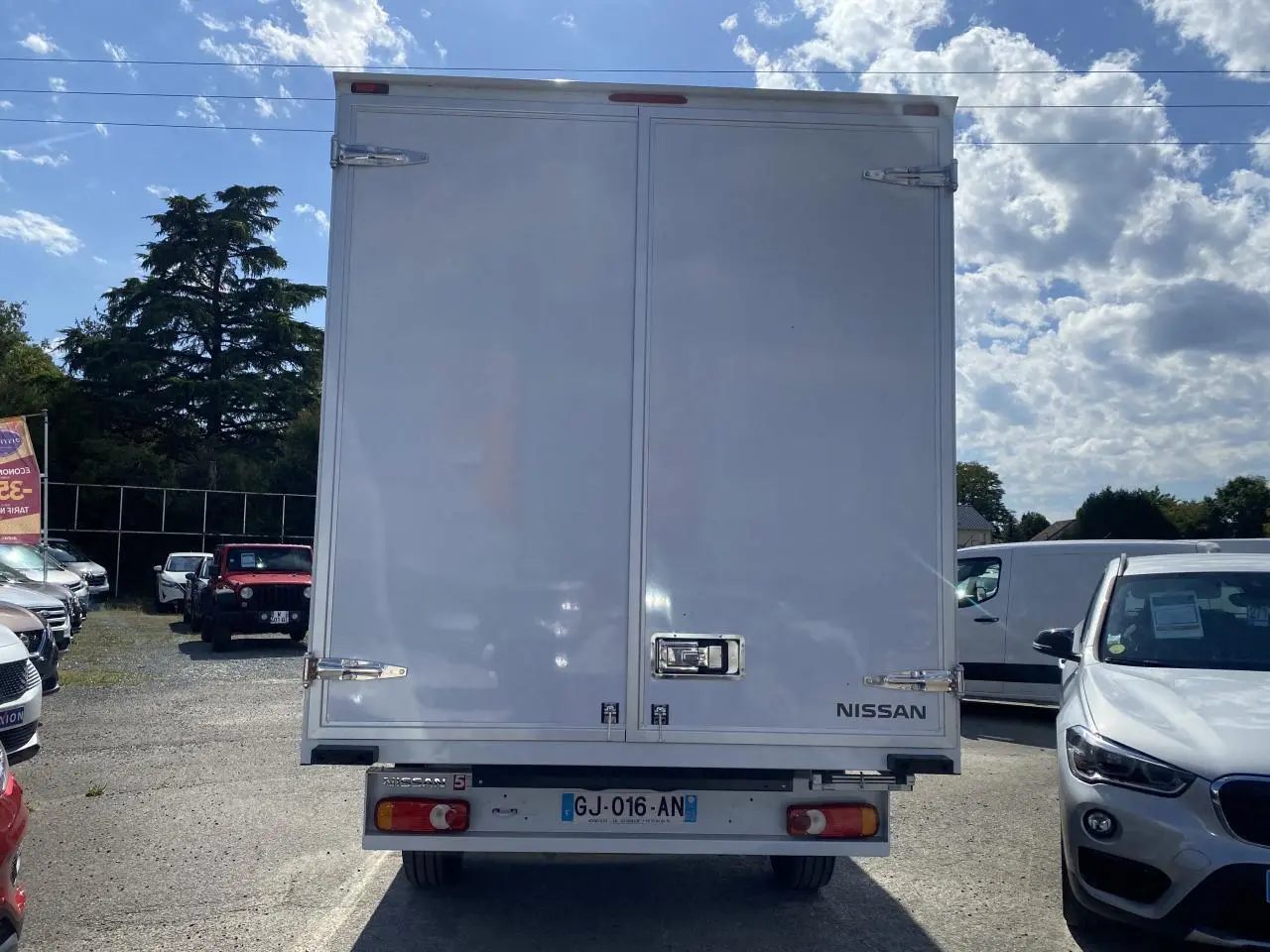 Vue arrière d'un utilitaire Nissan Interstar blanc avec caisse grand volume et portes fermées sous un ciel partiellement nuageux.