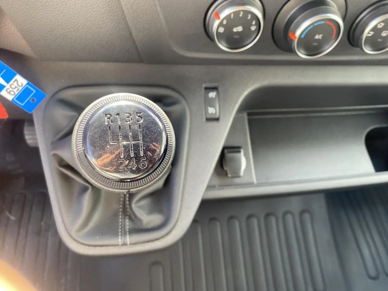 Gros plan sur le levier de vitesse manuel chromé du Nissan Interstar blanc avec commandes de climatisation en arrière-plan.