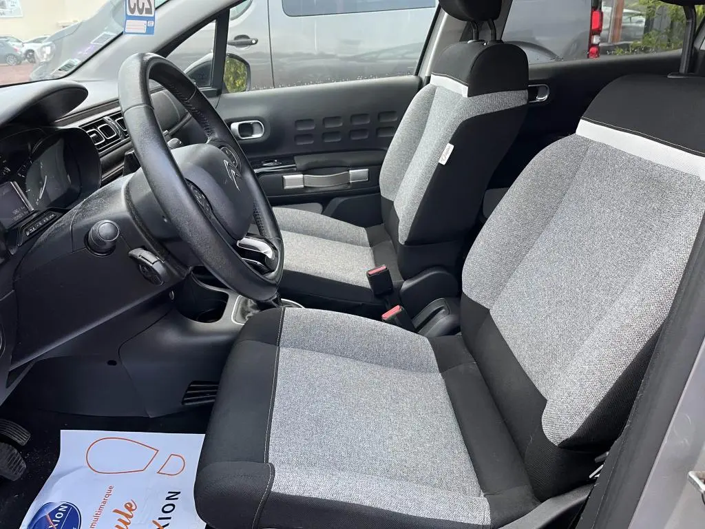 Vue intérieure côté conducteur de la Citroën C3 2019, sièges gris clair et noir avec volant noir visible.