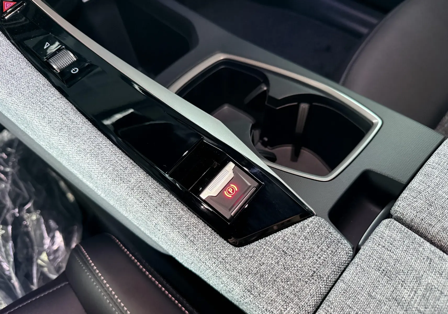 Gros plan sur la console centrale grise du Peugeot 3008 Hybrid 2025 avec bouton de frein à main électronique allumé.