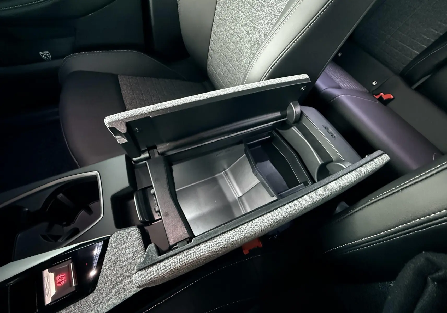 Intérieur du Peugeot 3008 Hybrid 2025 montrant la console centrale ouverte avec rangement et sièges tissu gris et cuir noir.