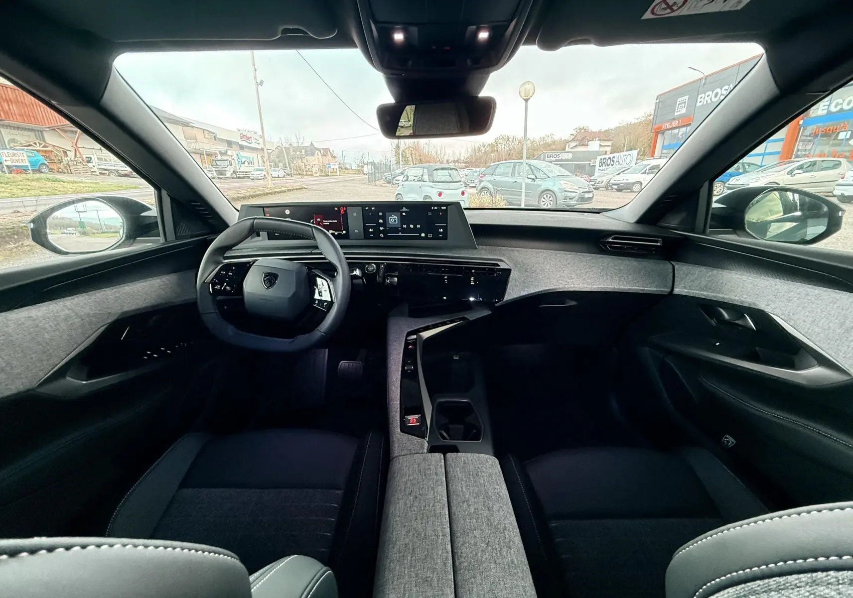 Vue intérieure avant du Peugeot 3008 Hybrid 2025, tableau de bord moderne avec écran large et finition tissu gris.