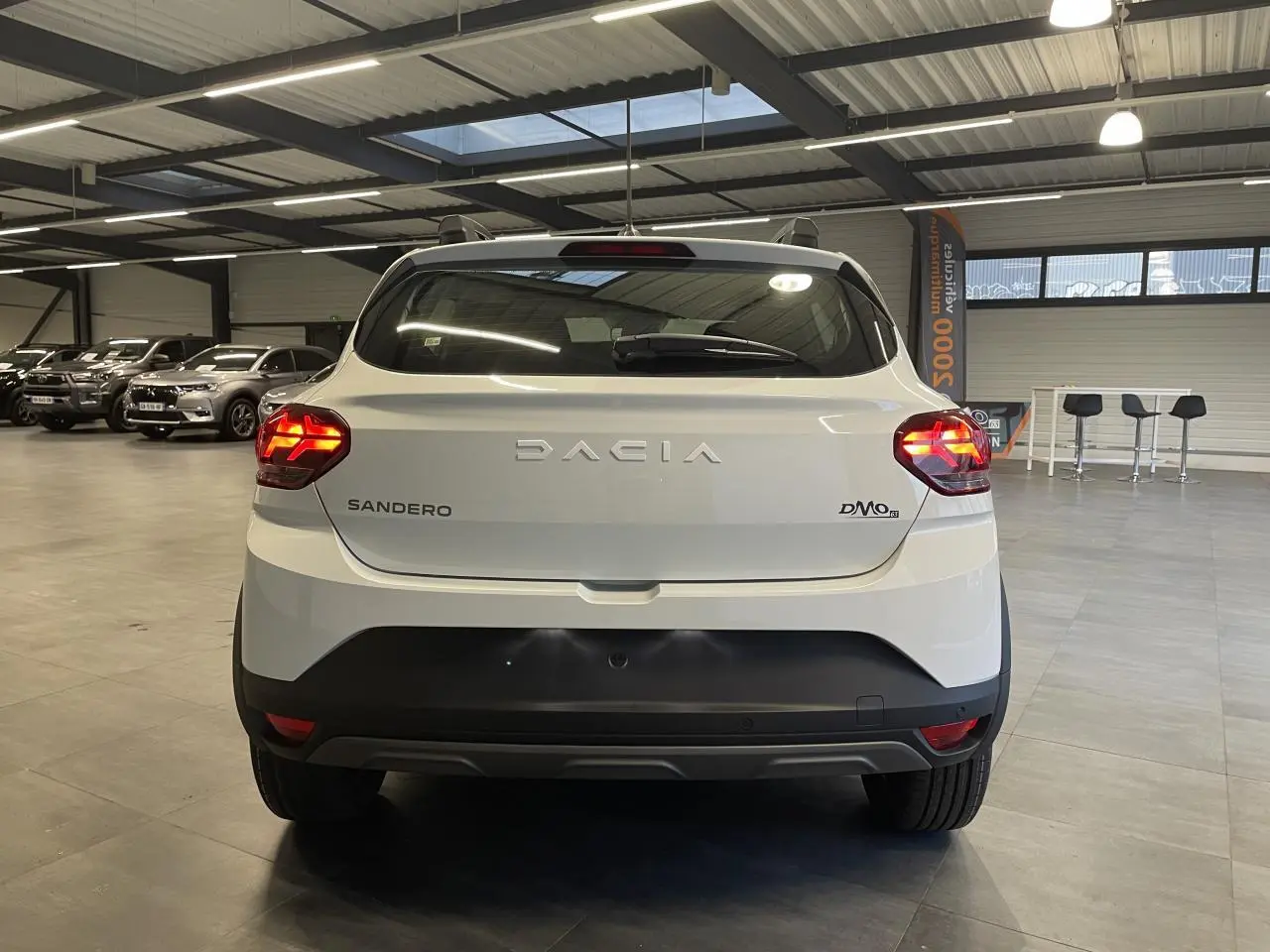 Vue arrière d'une Dacia Sandero TCe 90 Stepway blanche Glacier en intérieur avec feux arrière allumés.