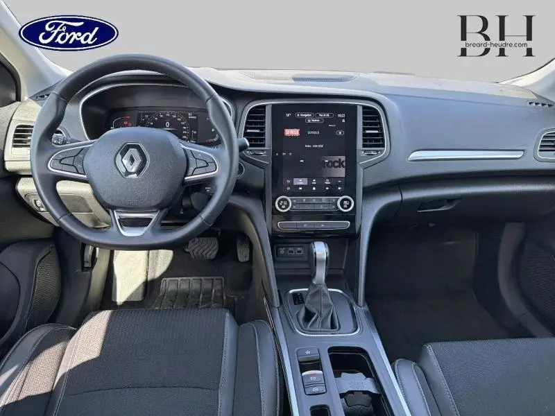 Vue intérieure avant de la Renault Mégane gris Highland 2023, mettant en valeur le volant multifonction et l'écran tactile central vertical.