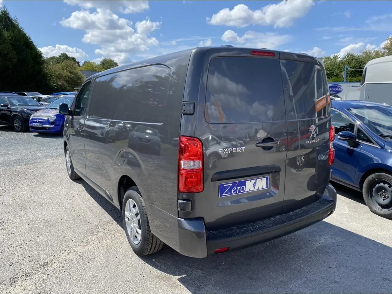 Vue 3/4 arrière droite d'un Peugeot Expert Fourgon gris platinium avec portes arrière tôlées et plaque Zero KM visible