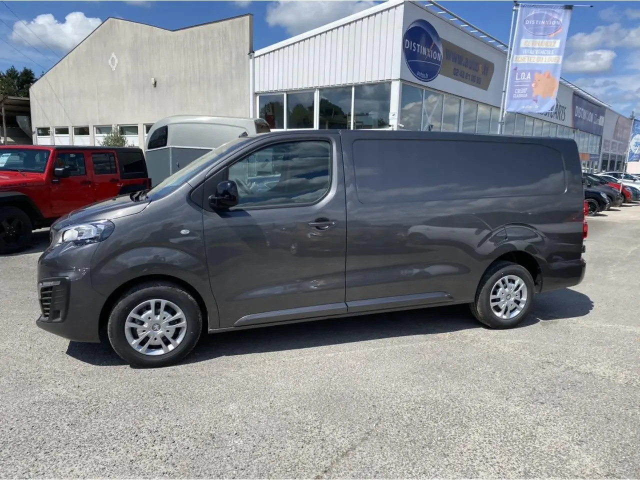Vue latérale droite d'un Peugeot Expert Fourgon gris platinium stationné devant un bâtiment commercial.