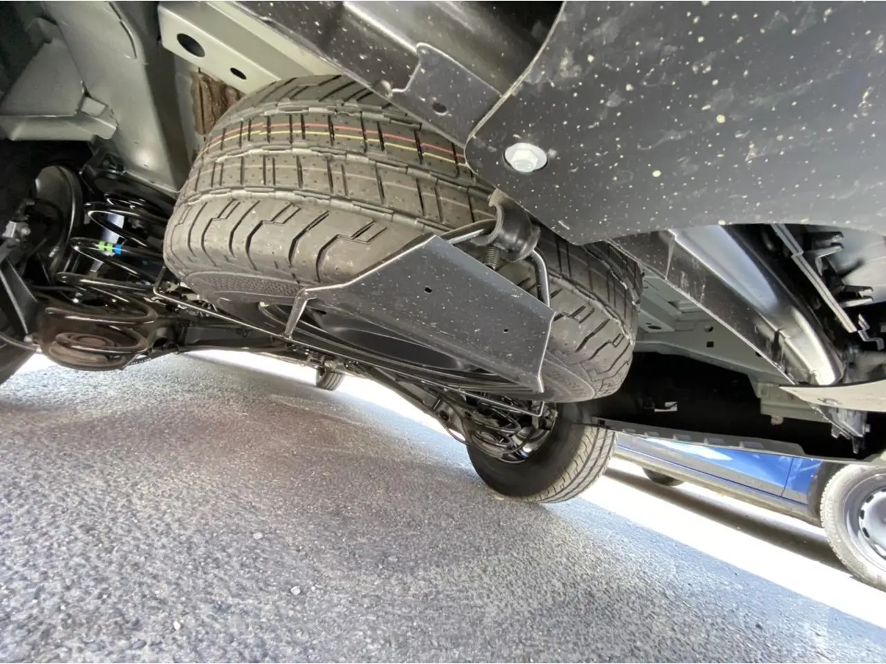 Vue en contre-plongée sous un Peugeot Expert Fourgon gris platinium, montrant la roue de secours sous le châssis.