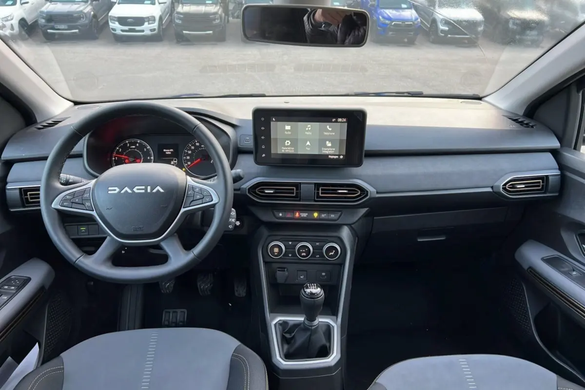 Vue intérieure avant du Dacia Sandero Stepway 2024, tableau de bord moderne avec écran tactile et levier de vitesses manuel.