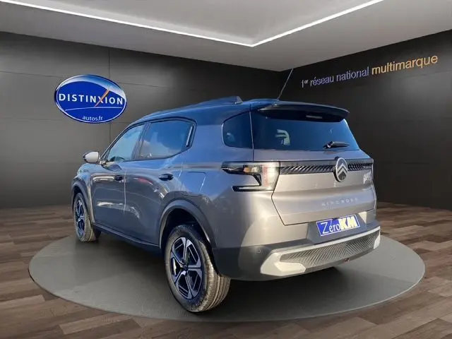Vue 3/4 arrière droite d'un Citroën C3 Aircross Hybrid 145 gris Mercury avec toit noir, en intérieur showroom.