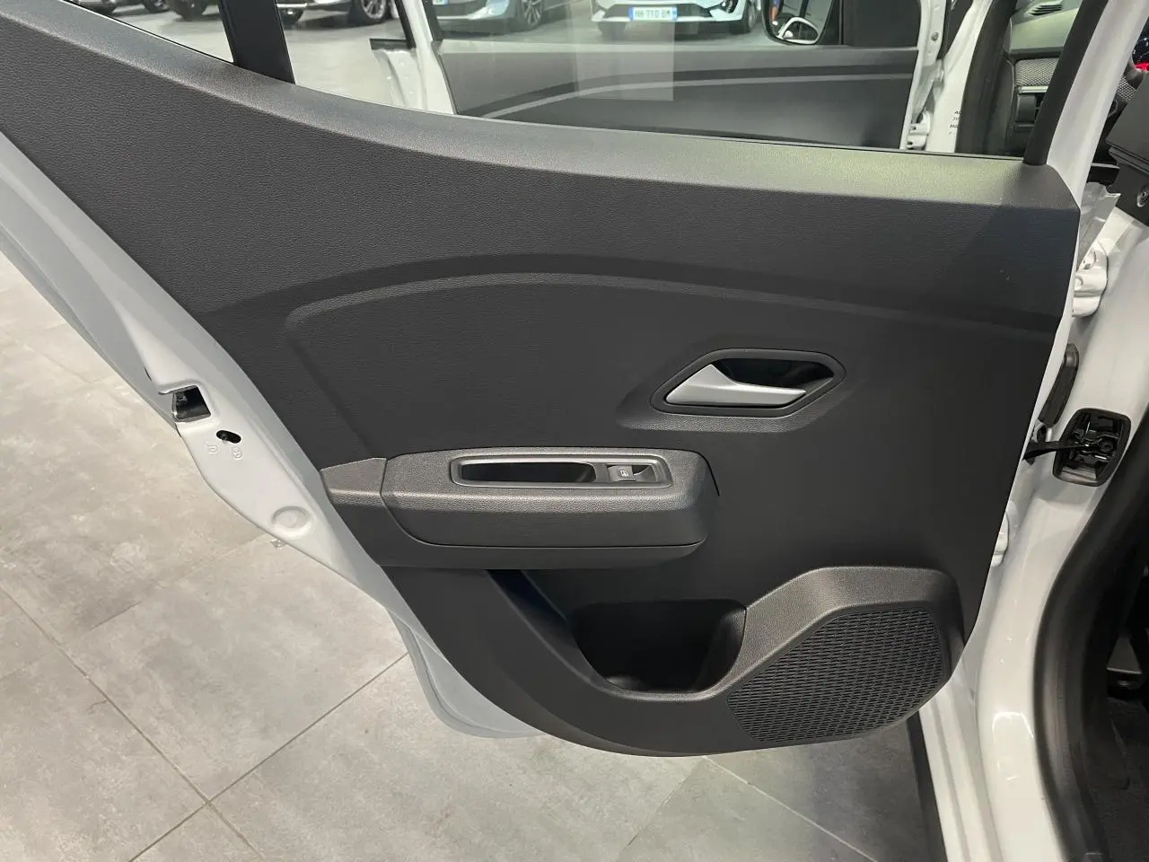 Vue rapprochée de la porte arrière gauche noire du Dacia Sandero Stepway blanc glacier 2025 avec bouton de vitre électrique.