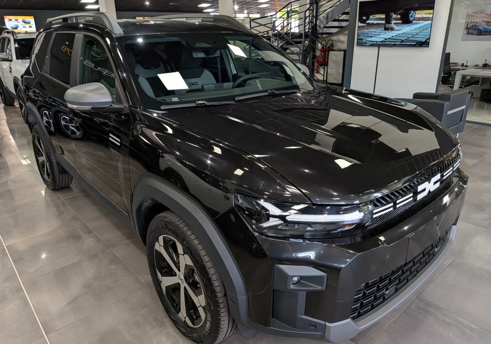 Dacia Bigster noir nacré en 3/4 avant droit, avec calandre distinctive et jantes bicolores en showroom.