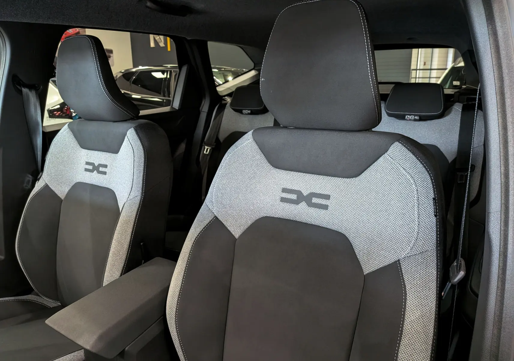 Vue intérieure rapprochée des sièges avant tissu gris et noir du Dacia Bigster 2026 avec logo brodé sur appuie-tête.