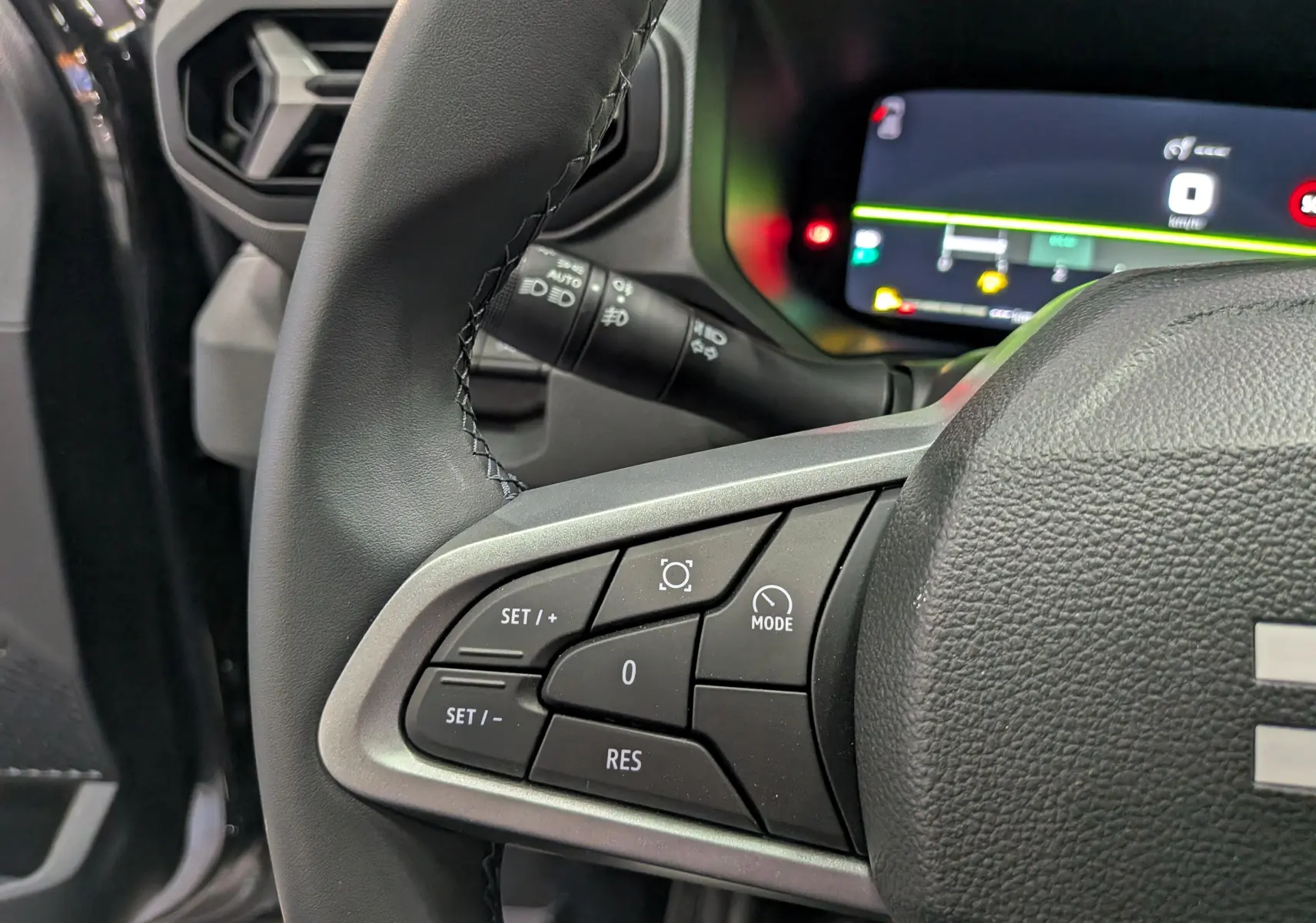Gros plan sur les commandes au volant du Dacia Bigster 2026, intérieur noir avec affichage numérique en arrière-plan.