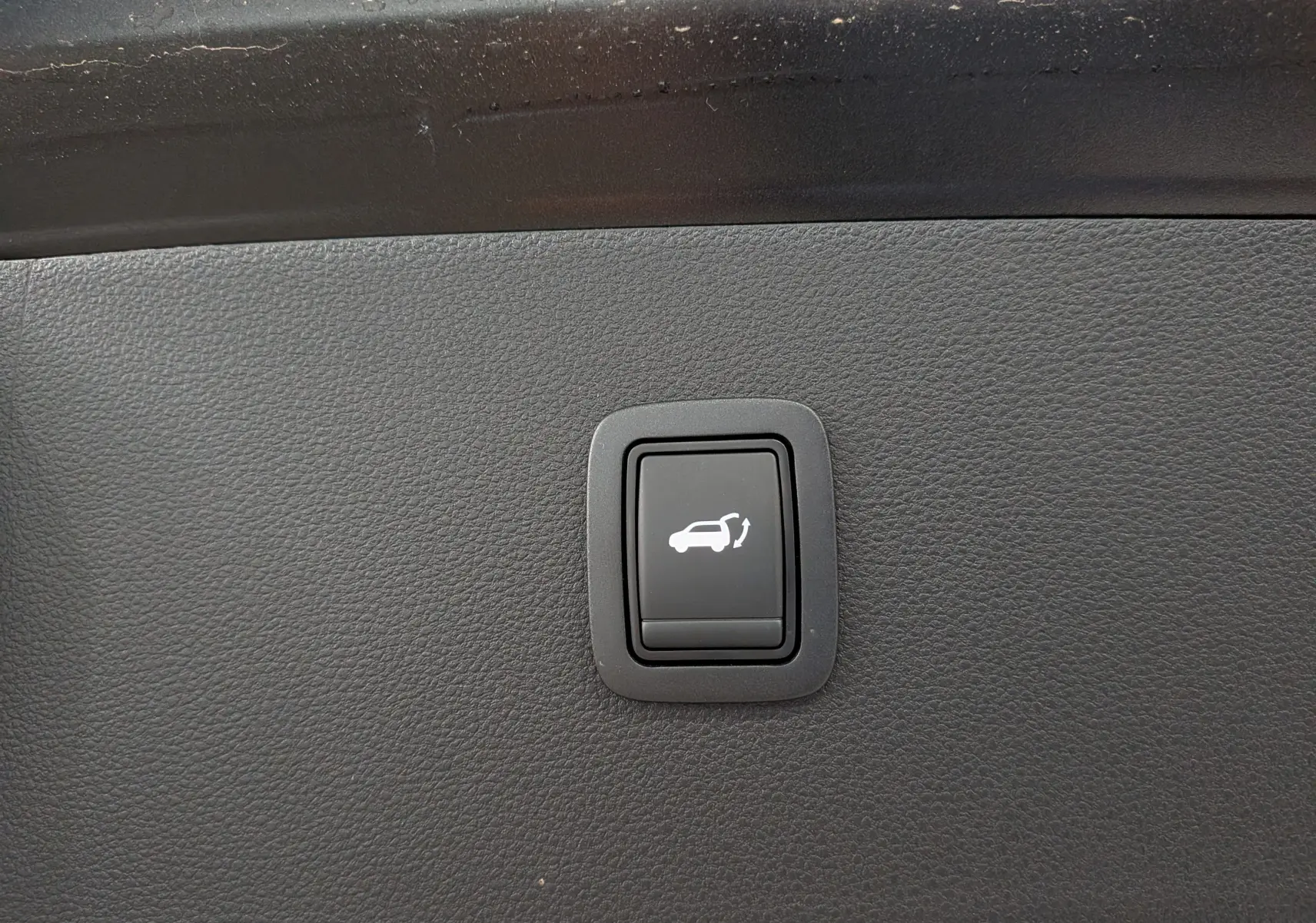 Bouton noir de commande d'ouverture électrique du coffre sur tableau de bord intérieur d'un Dacia Bigster noir nacré.