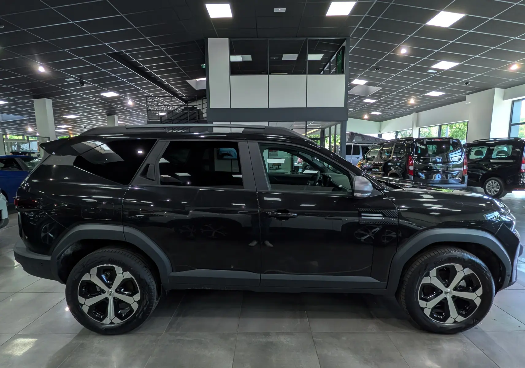Vue de profil côté gauche d'un Dacia Bigster noir nacré 2026 en showroom, avec jantes bi-ton distinctives.