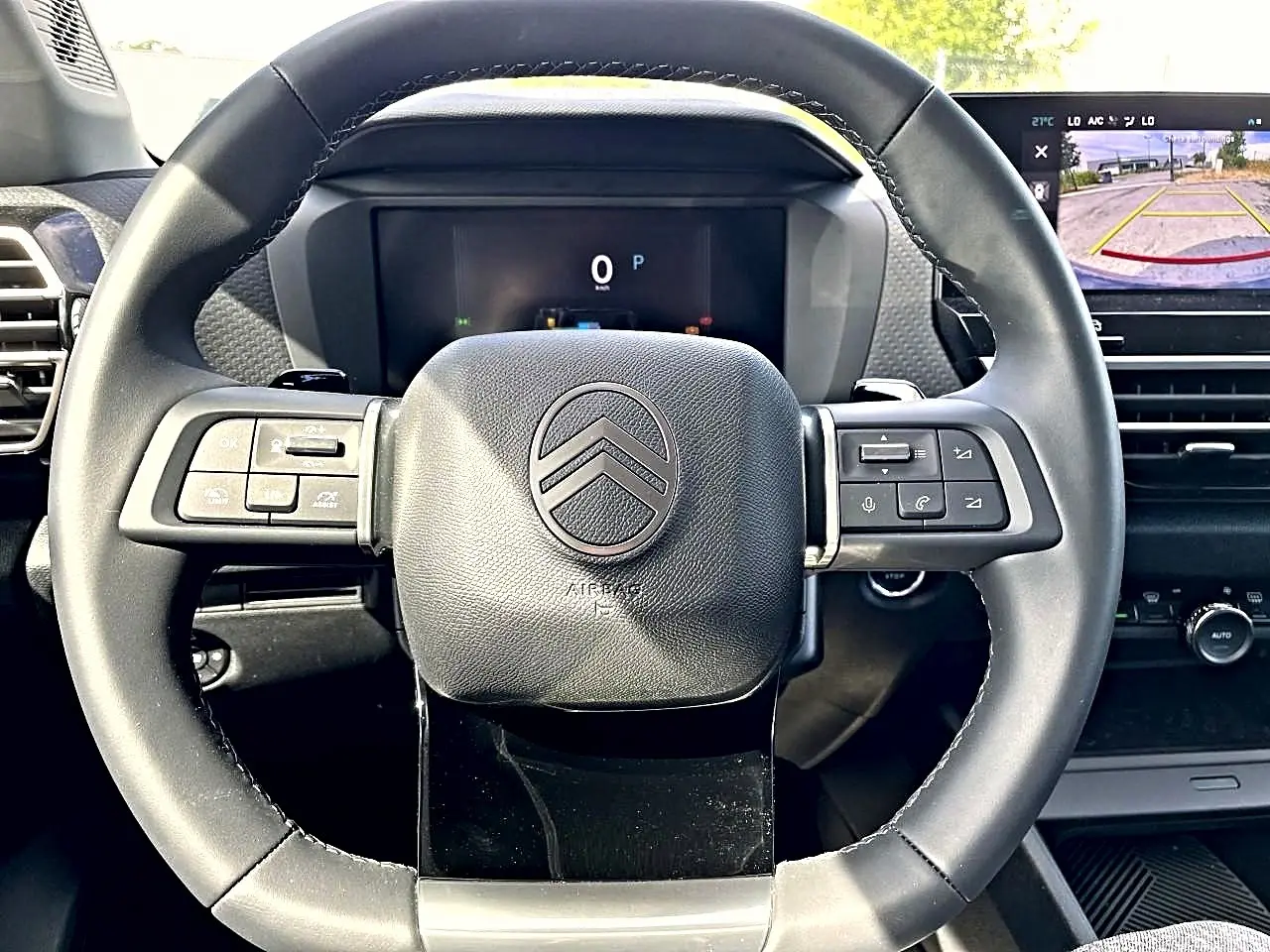 Vue rapprochée du volant cuir noir de la Citroën C4 X 2025 avec commandes intégrées et écran de caméra de recul visible.
