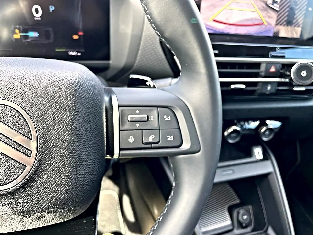 Gros plan sur le volant cuir noir et les commandes vocales du Citroën C4 X hybride 2025, avec écran tactile en arrière-plan.
