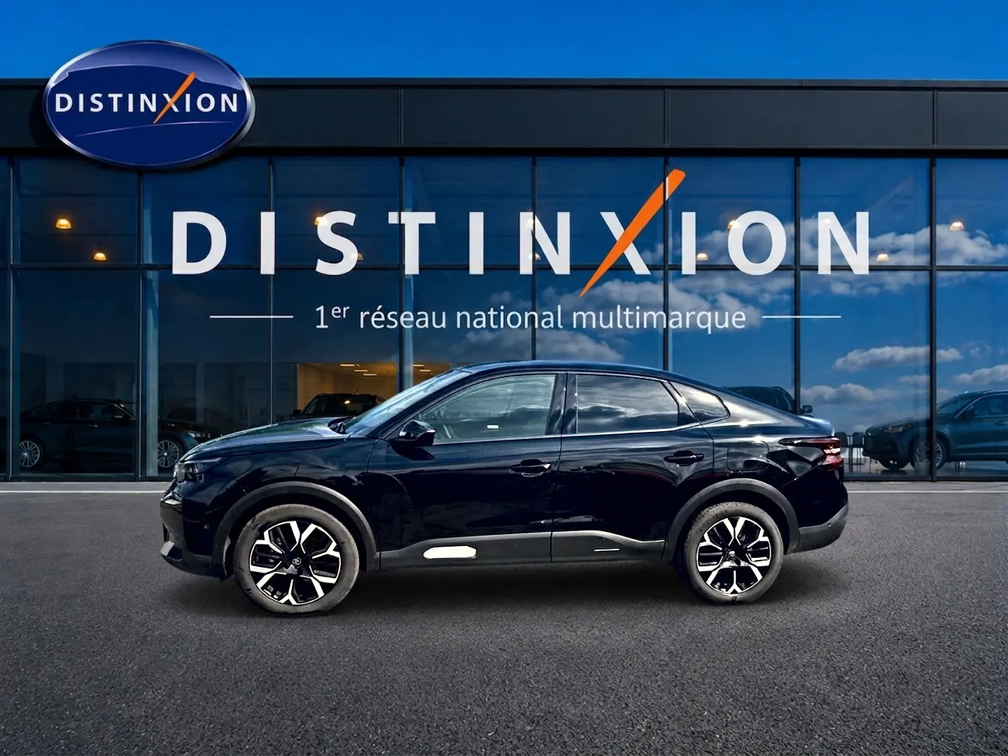 Profil droit de la Citroën C4 X noire 2025, avec jantes alu distinctives, devant une vitrine vitrée bleue.