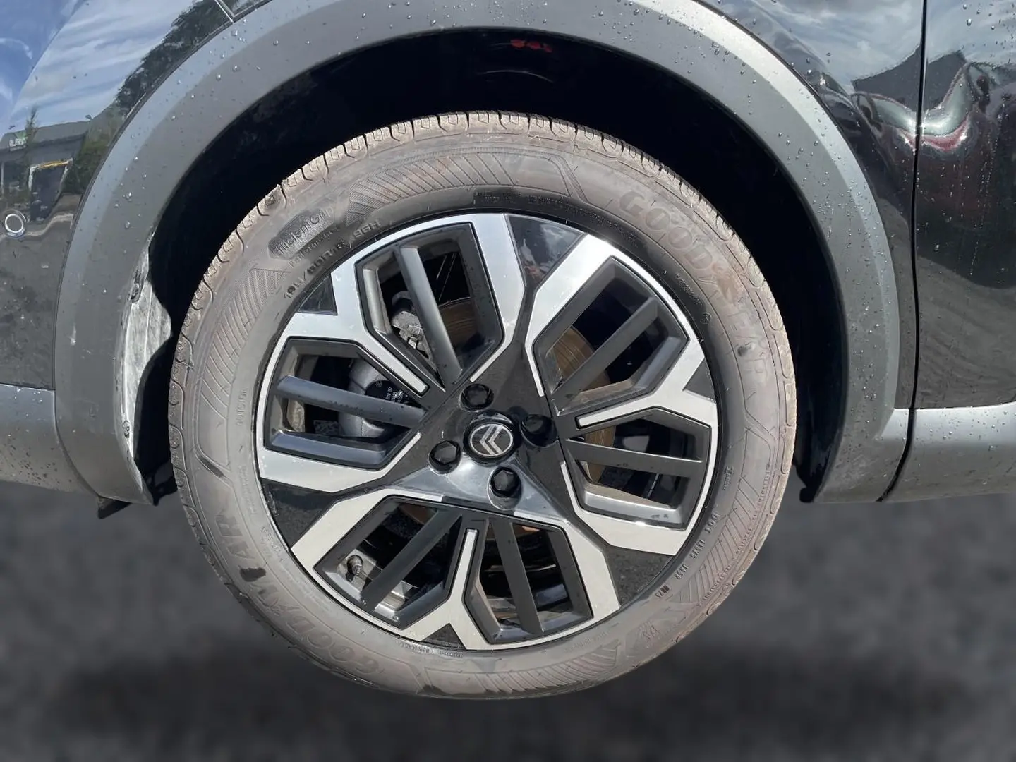 Gros plan sur la jante alu noire et argentée d'une Citroën C4 X noire, mettant en valeur le logo Citroën central.