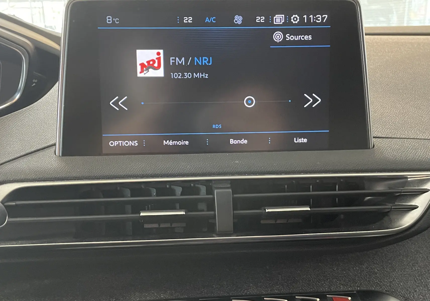 Écran central tactile du tableau de bord du Peugeot 5008 blanc nacré, affichant la radio FM NRJ à 102.30 MHz.