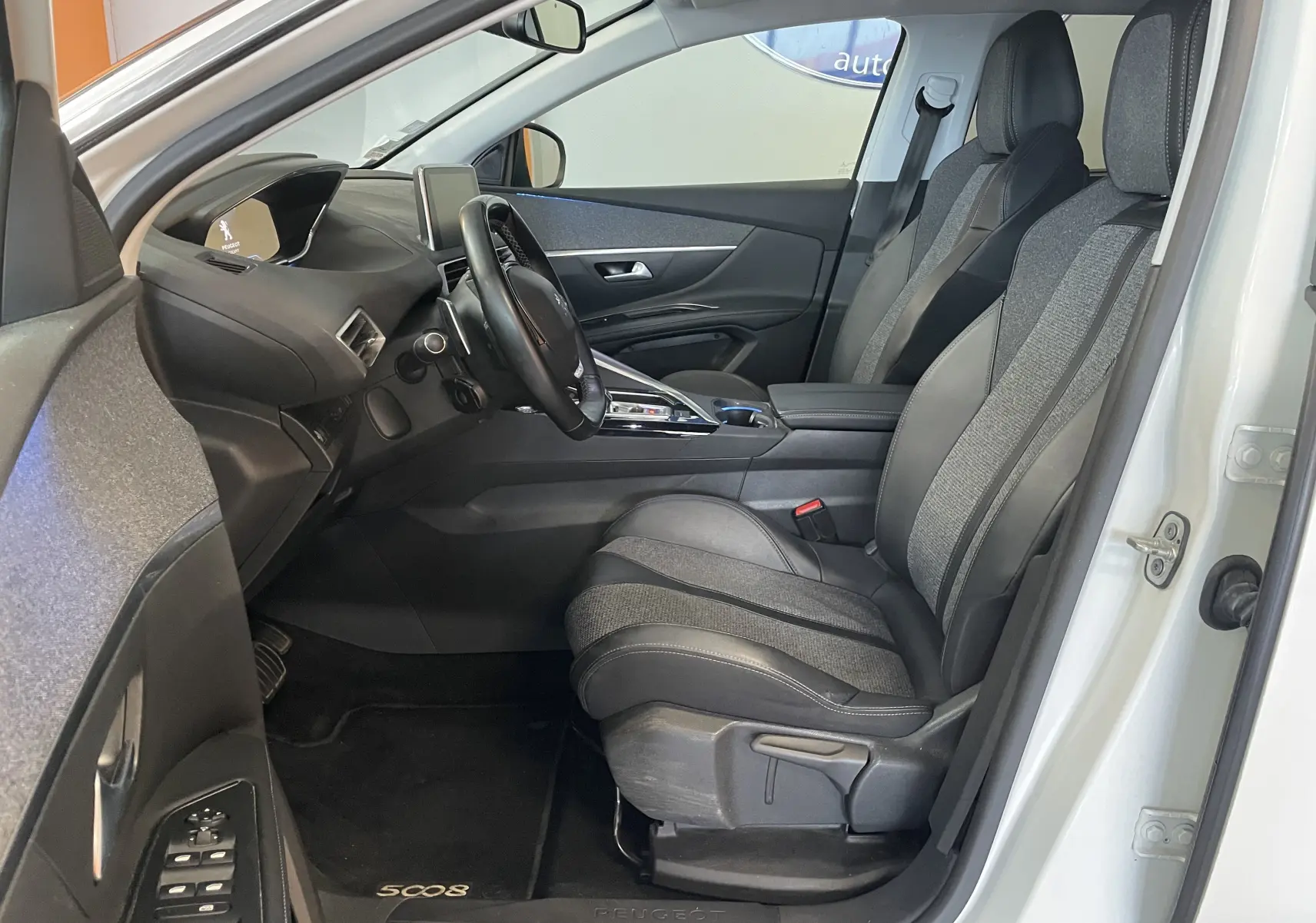 Vue intérieure côté conducteur du Peugeot 5008 blanc nacré 2019, sièges tissu et cuir, tableau de bord moderne avec écran central.