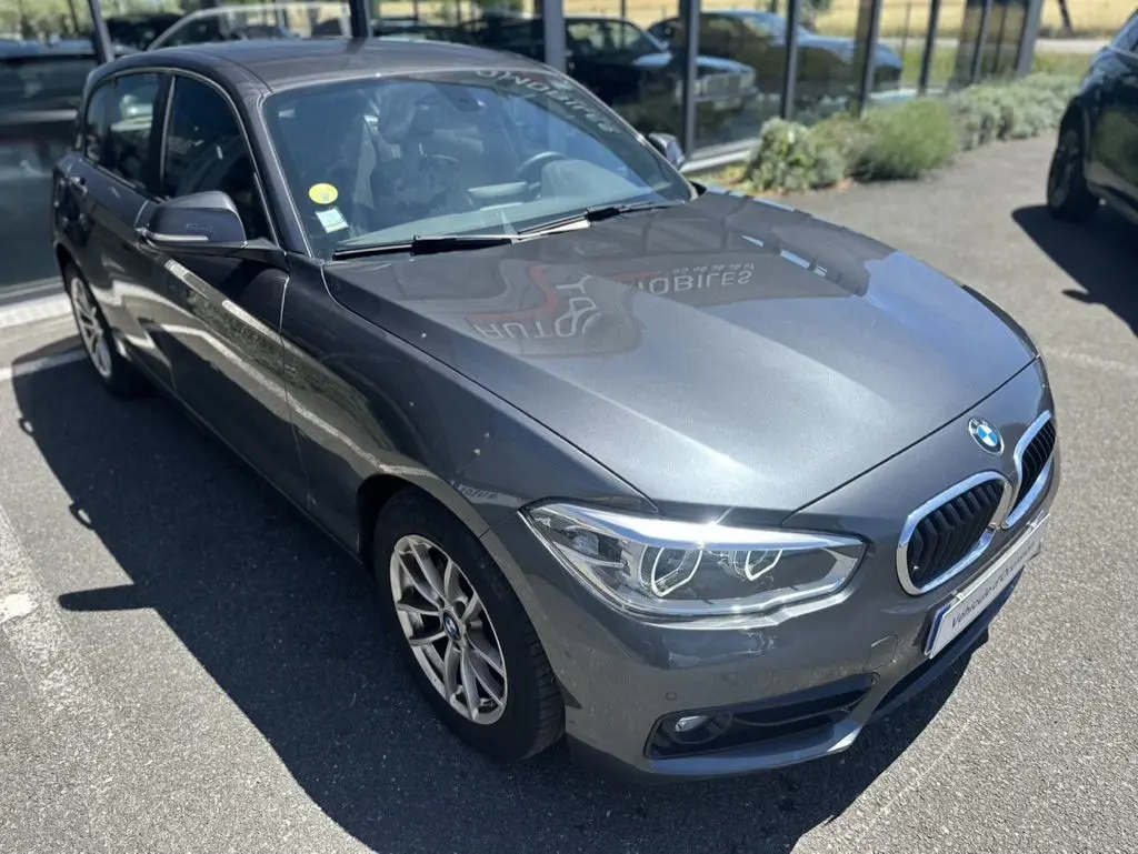 BMW Série 1 F20 gris foncé vue 3/4 avant droit, avec phares LED et calandre double haricot chromée.