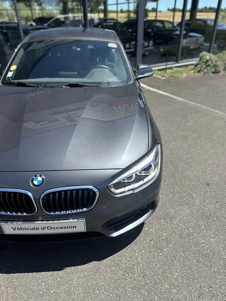 Vue 3/4 avant droite d'une BMW Série 1 F20 gris foncé avec calandre double haricot et phares LED visibles.