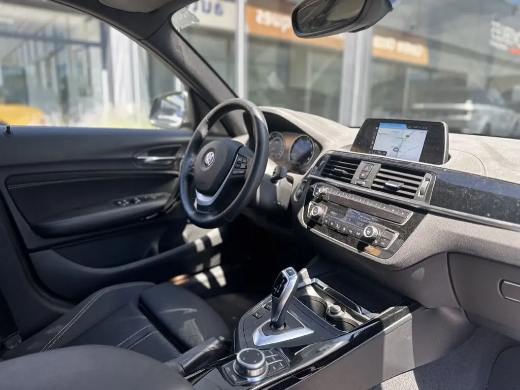 Vue intérieure côté conducteur de la BMW Série 1 F20 gris foncé, avec tableau de bord et écran de navigation visible.