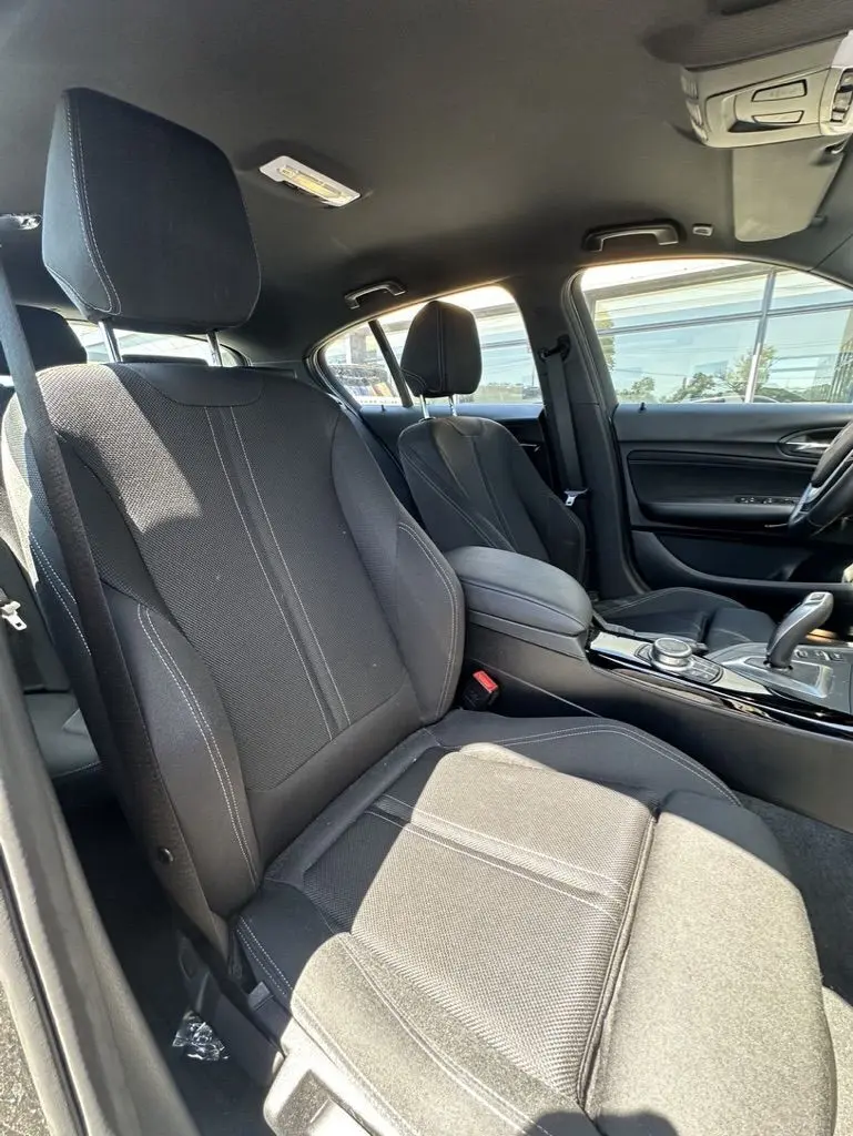 Vue intérieure côté conducteur de la BMW Série 1 F20 116D 2019 avec sièges tissu noirs et console centrale brillante.