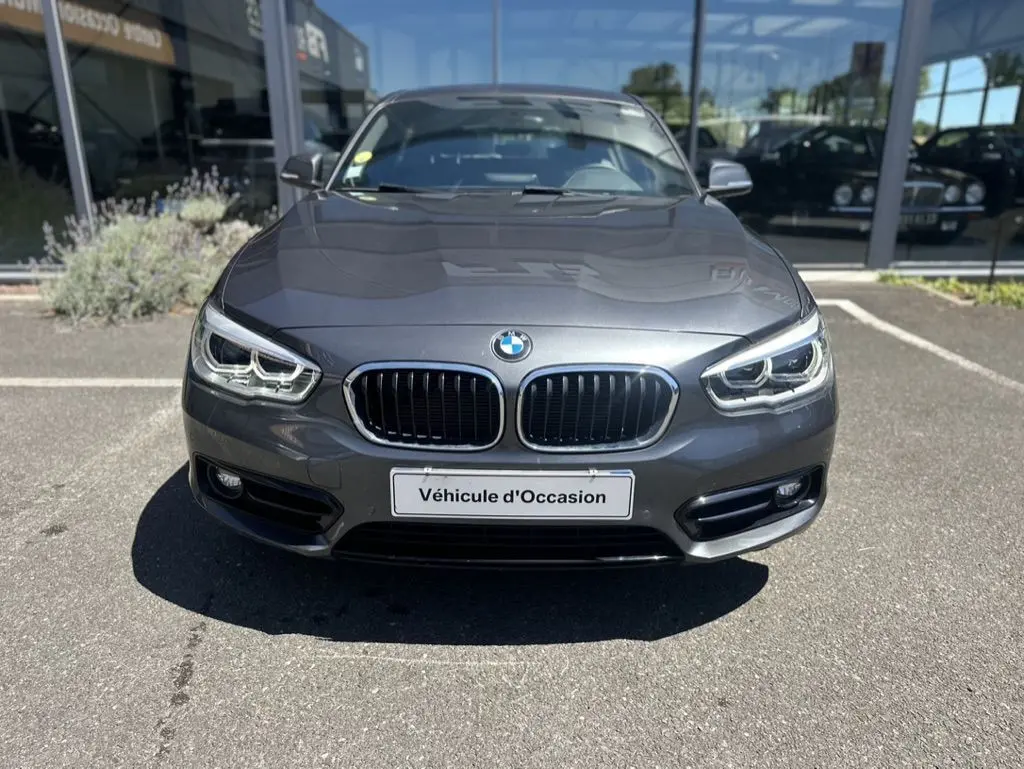 Vue frontale d'une BMW Série 1 F20 gris foncé de 2019 avec calandre double haricot et phares LED, en vente d'occasion.