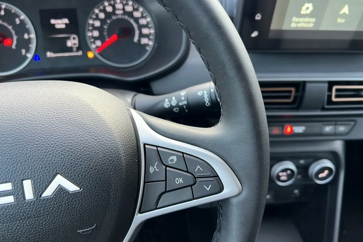 Gros plan sur le volant et le tableau de bord du Dacia Sandero Stepway Bleu iron 2024, avec commandes multifonctions visibles.