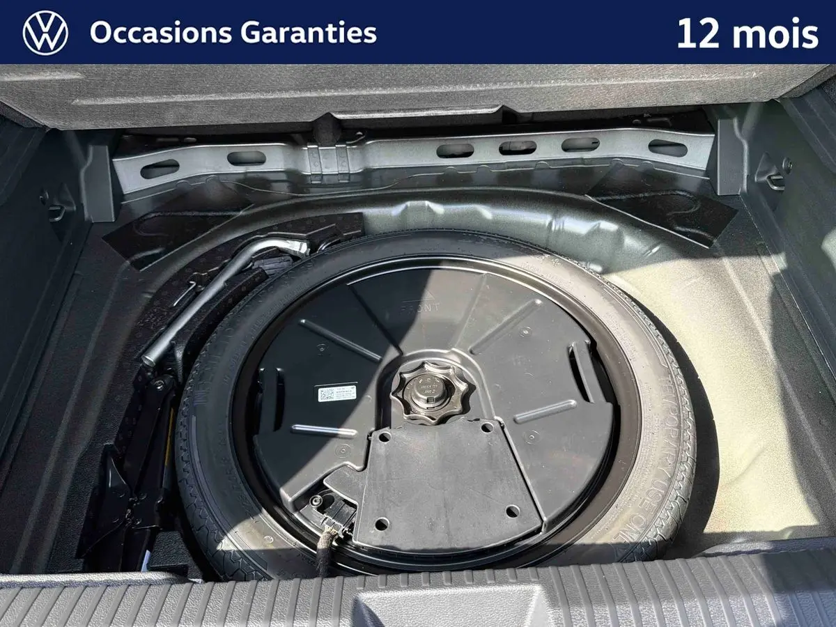 Gros plan sur la roue de secours et le cric dans le coffre ouvert d’un Volkswagen T-Roc noir.