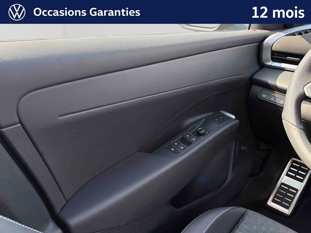 Vue intérieure côté gauche de la porte avant noire du Volkswagen T-Roc 2026 avec commandes électriques et volant partiel visible.