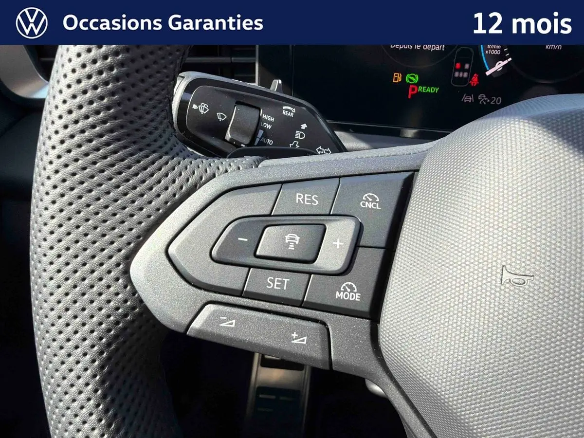 Gros plan sur le volant multifonction perforé du Volkswagen T-Roc noir, avec commandes de régulateur de vitesse et assistant de conduite.