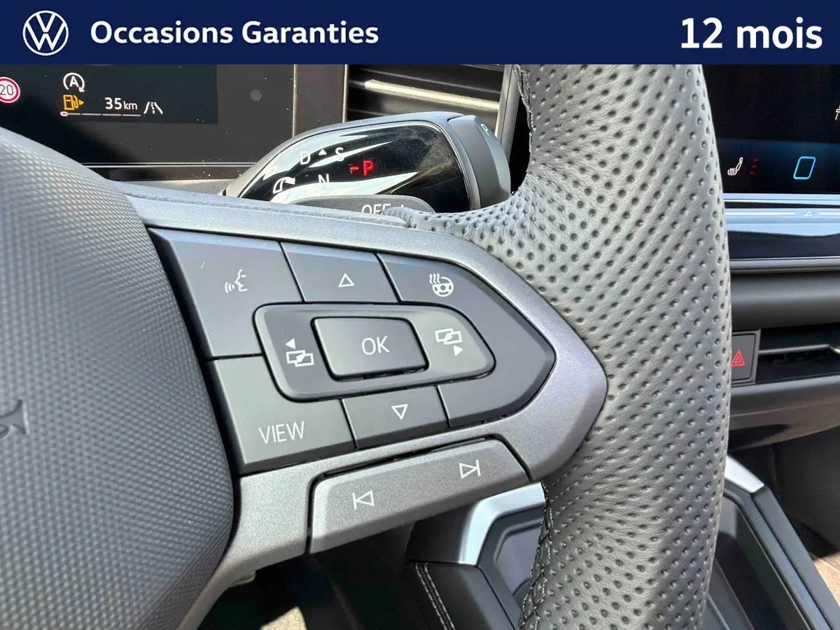 Gros plan sur le volant perforé avec commandes multifonctions du Volkswagen T-Roc noir, intérieur moderne et écran digital visible.