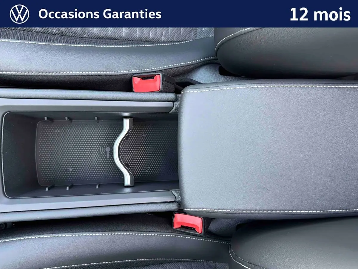 Vue plongeante sur la console centrale noire du Volkswagen T-Roc avec accoudoir et rangements ouverts.