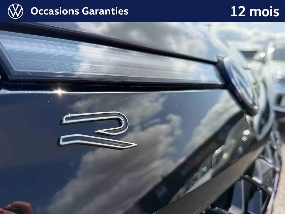Gros plan sur l'avant noir brillant d'un Volkswagen T-Roc avec logo "R" et calandre détaillée en reflet.