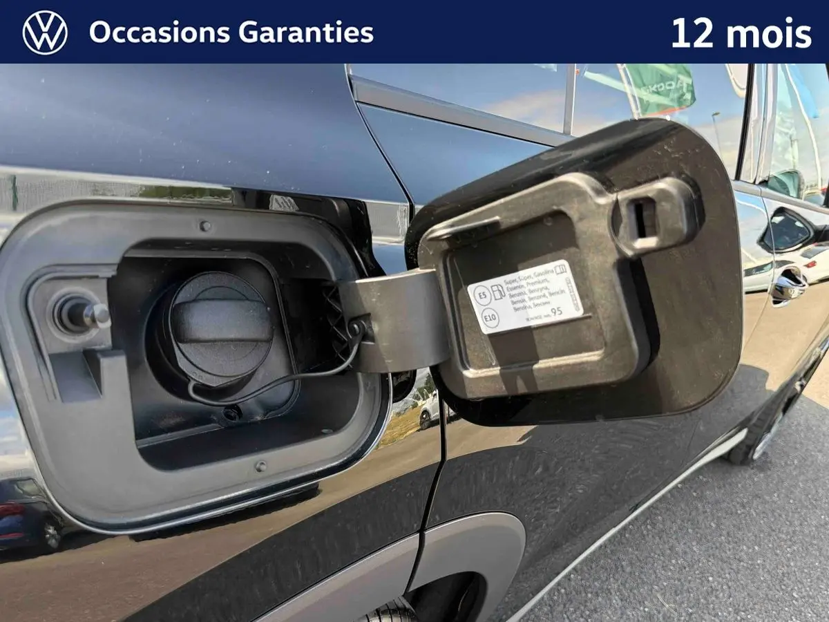 Vue rapprochée du côté gauche d’un Volkswagen T-Roc noir montrant la trappe à carburant ouverte sur un parking.