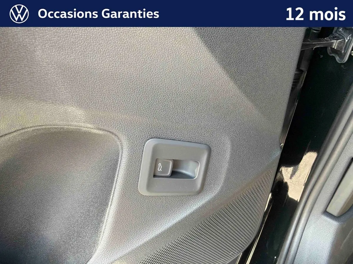 Détail du bouton d'ouverture électrique du coffre sur la porte arrière droite d'un Volkswagen T-Roc noir.