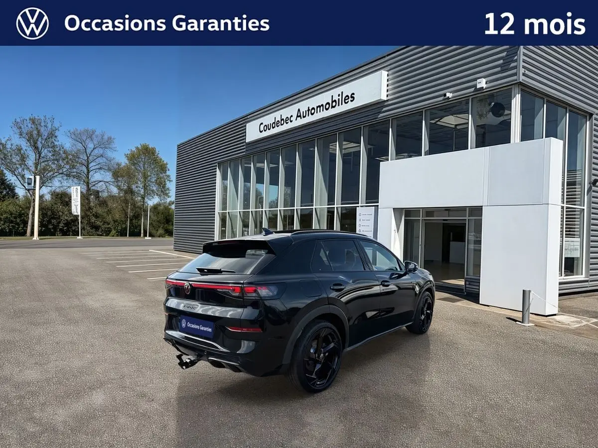 Volkswagen T-Roc noir en 3/4 arrière droit, avec jantes noires sport et crochet d'attelage escamotable visible.
